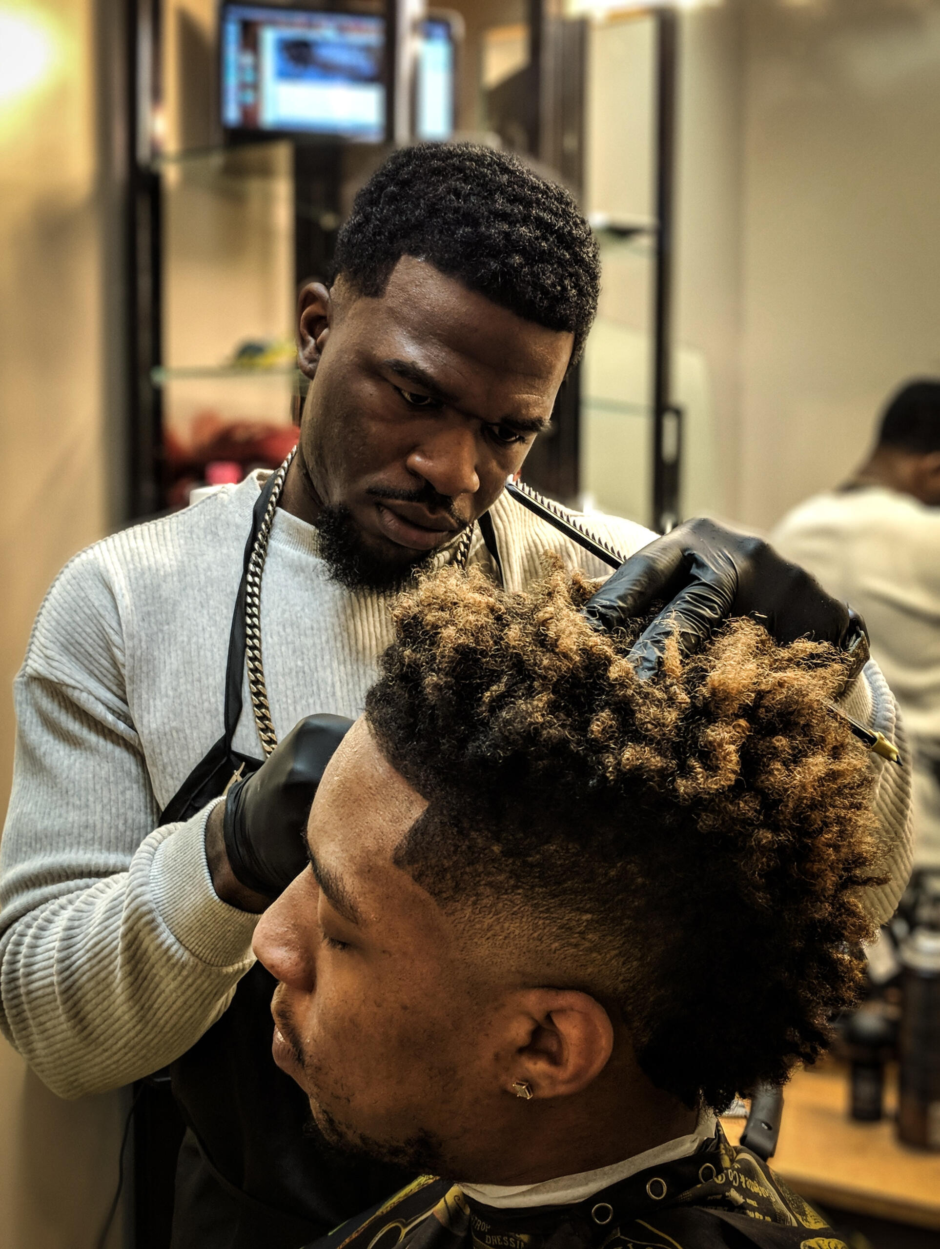 One African American man getting his hair cut by another African American man in a barber shop for African Americans.
