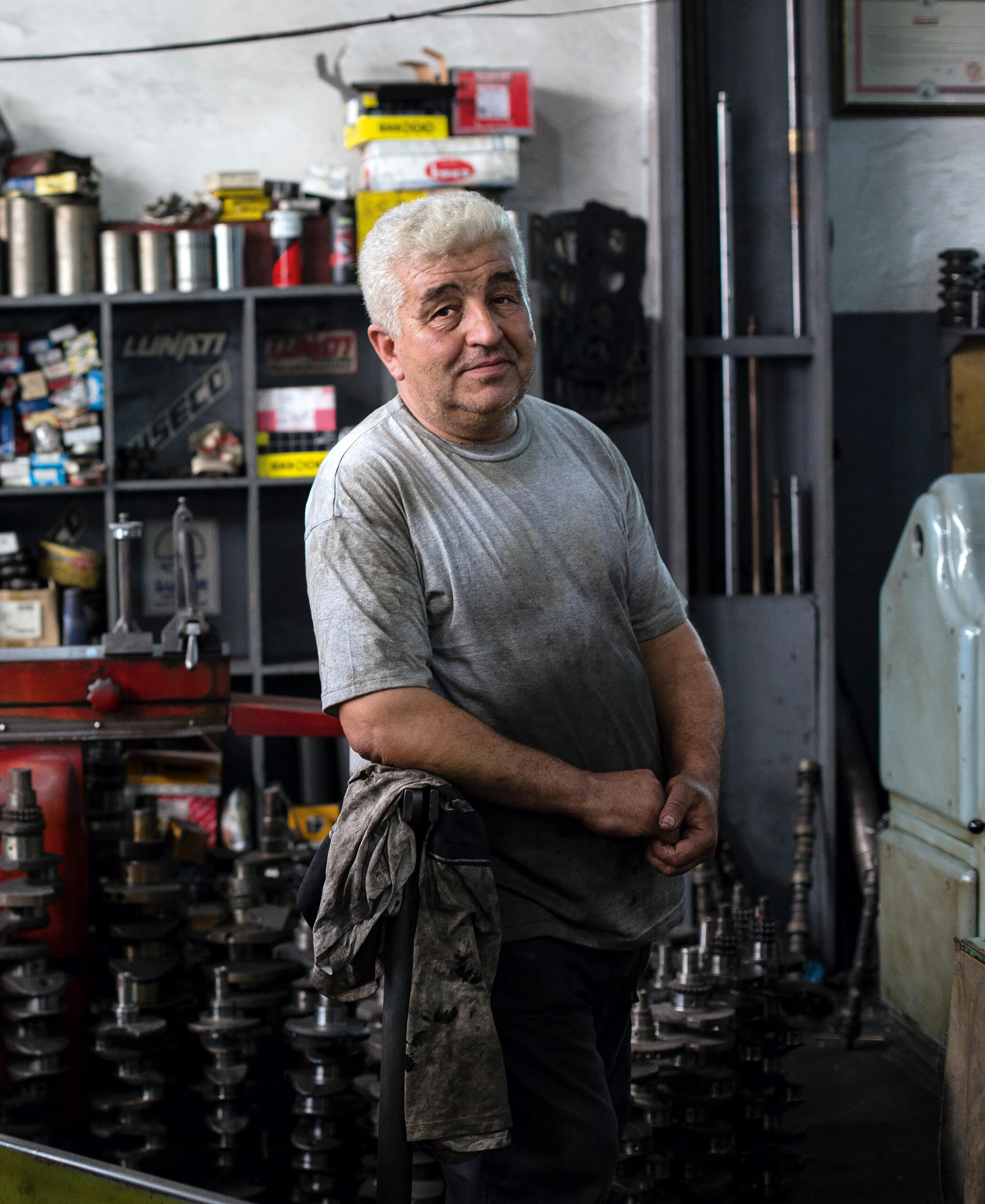An older man with silver hair. He's probably a mechanic. He's covered in grease and posing among car parts.