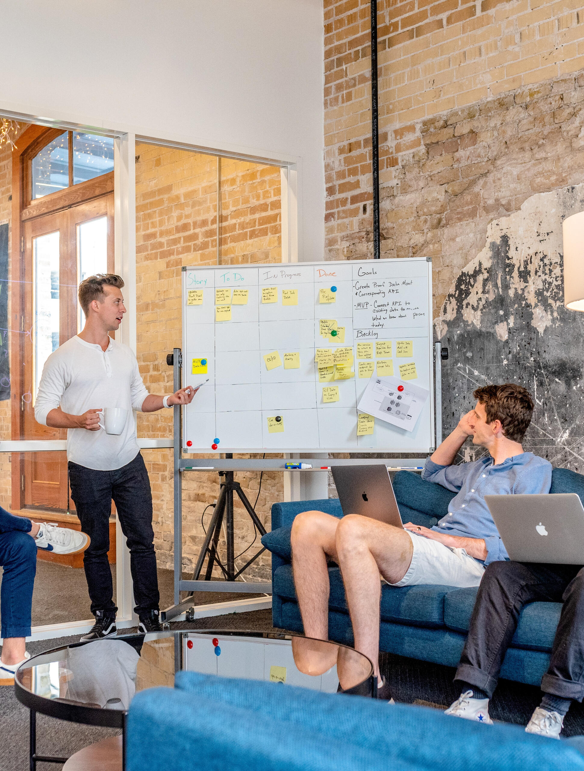 African American woman standing with an Apple iPad in her right hand and her left hand on her hip. She's wearing jeans, a white shirt, and a yellow blazer over top.