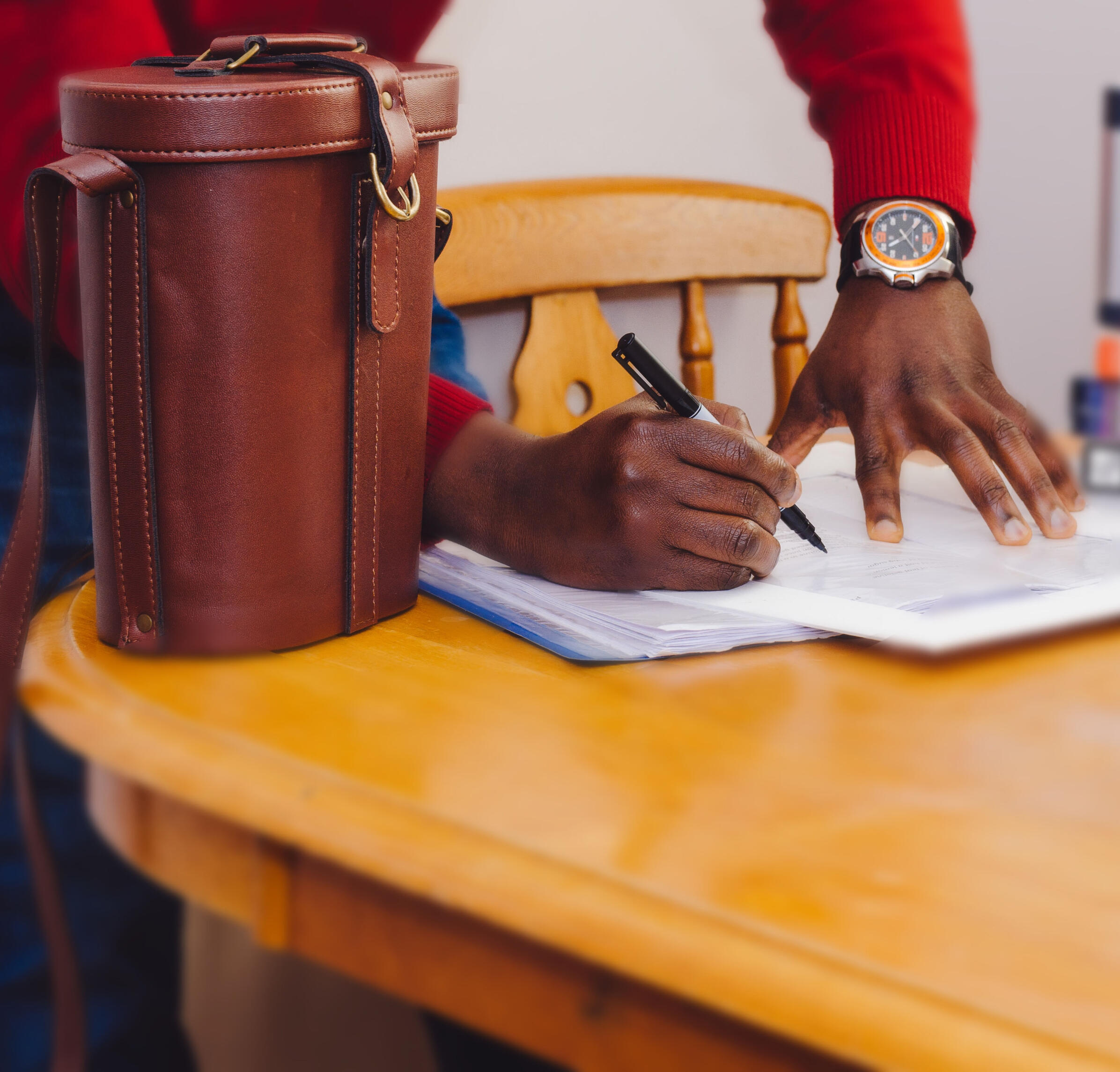 African American human using an ink pen to sign some documents on a nice wooden kitchen table.